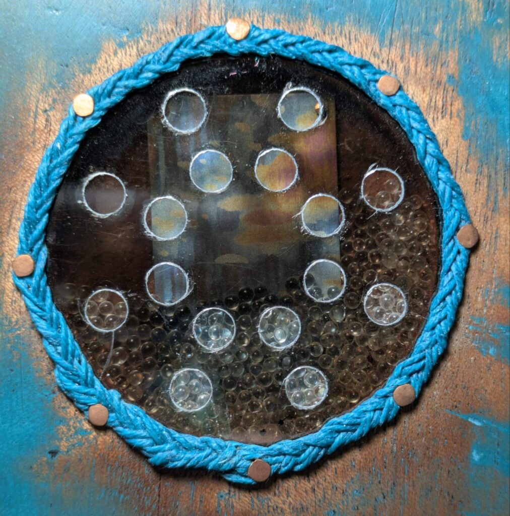 Colorful piece of niobium partially visible behind a round piece of mica with circular cutouts.