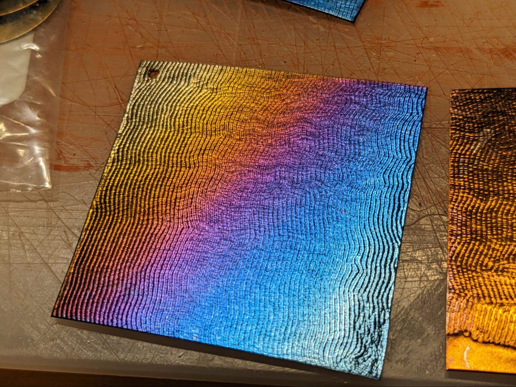 Square piece of metal with wavy texture and a diagonal gradient of bold colors.